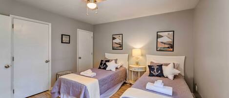 A hotel room with two beds, a ceiling fan, and artwork on the walls.