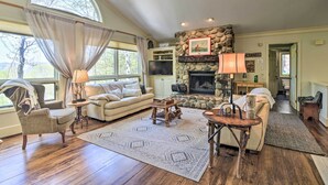 A spacious living room with a fireplace, a large window with curtains, a stone accent wall, and a cozy seating area. - Resort-style Harbor Springs Home Near Ski Resort! (Harbor Springs)