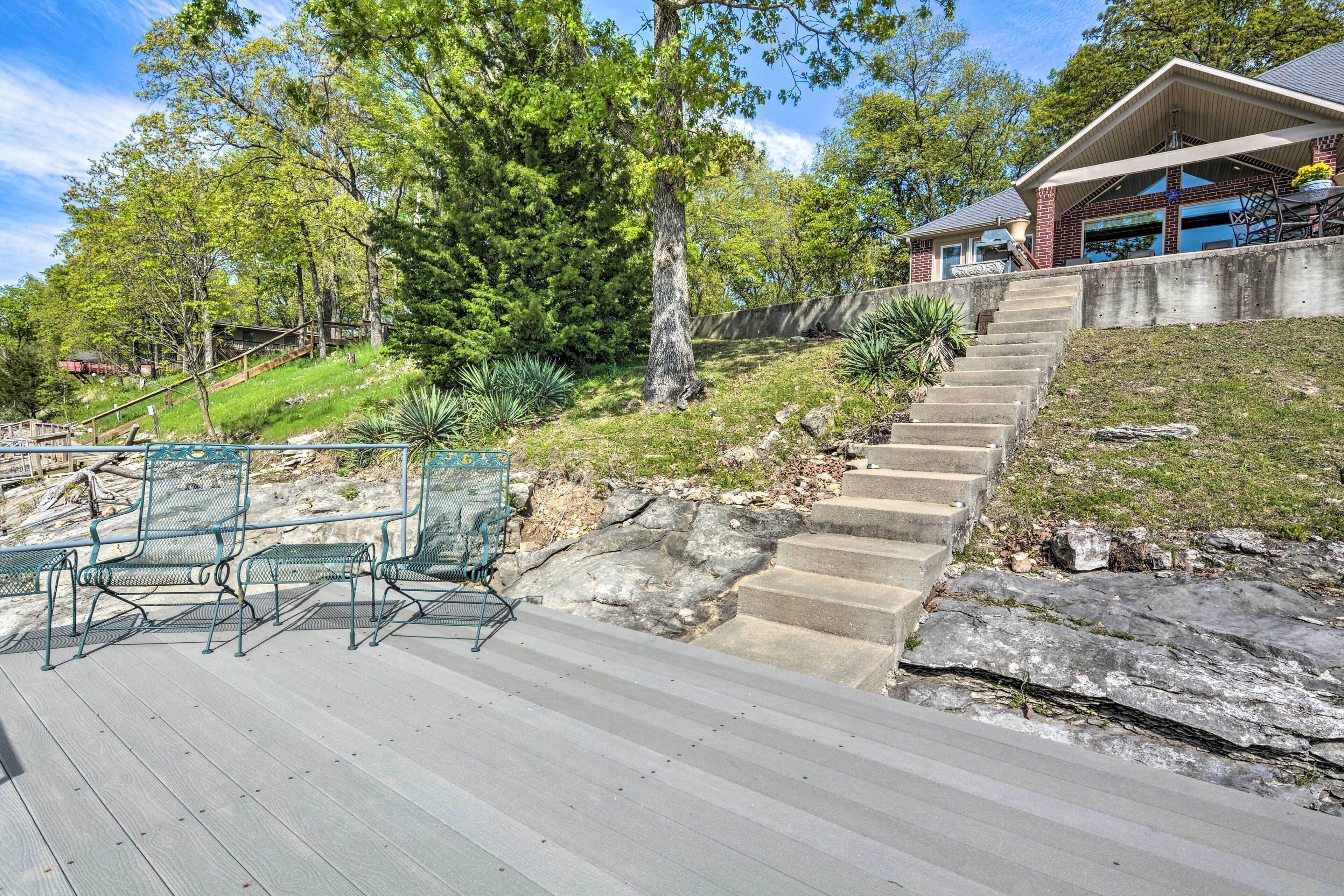 A wooden deck with outdoor furniture, a staircase leading to a house, and surrounding greenery.
