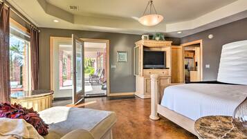 A spacious bedroom with a large bed, a seating area with a sofa and ottoman, a television, and a dining area visible through an open door.