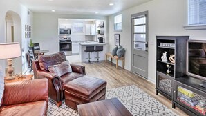 A modern living room with a leather sofa, a coffee table, and a TV stand. There is a kitchen in the background with white cabinets and a dining area. - Cozy Rapid City Retreat: Perfect for Exploring! (Rapid City)