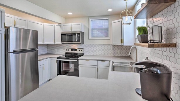 A modern kitchen with white cabinets, stainless steel appliances, a hexagonal tile backsplash, and a hanging light fixture. - Cozy Rapid City Retreat: Perfect for Exploring! (Rapid City)