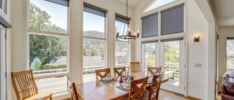 A dining area with a wooden table and chairs, large windows, and a ceiling fan.