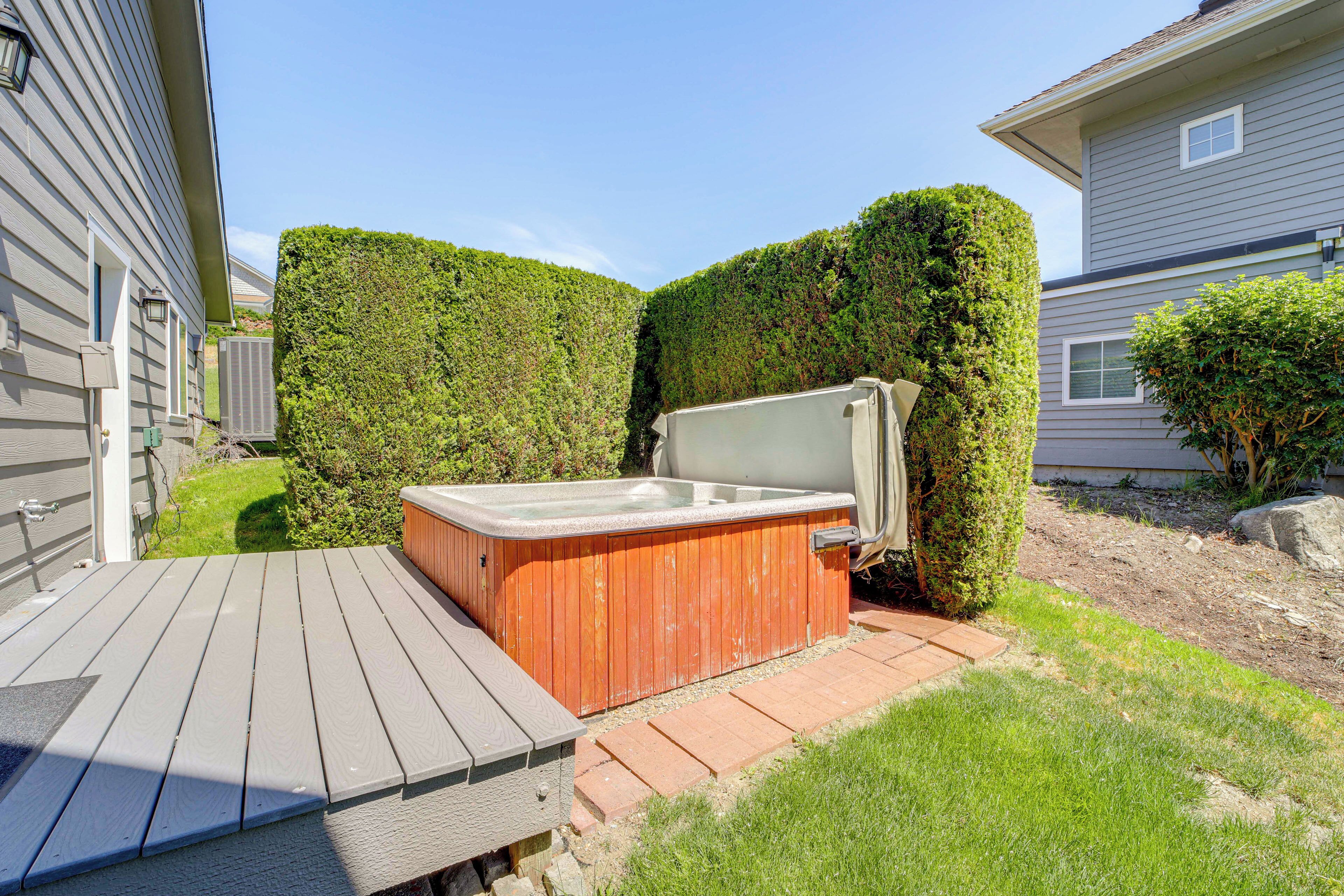 A wooden deck with a hot tub, surrounded by well-maintained hedges and a grassy area.