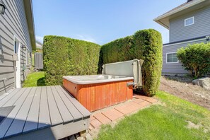 A wooden deck with a hot tub, surrounded by well-maintained hedges and a grassy area. - Modern Retreat w/ Hot Tub - Steps to Lake Chelan! (Manson)
