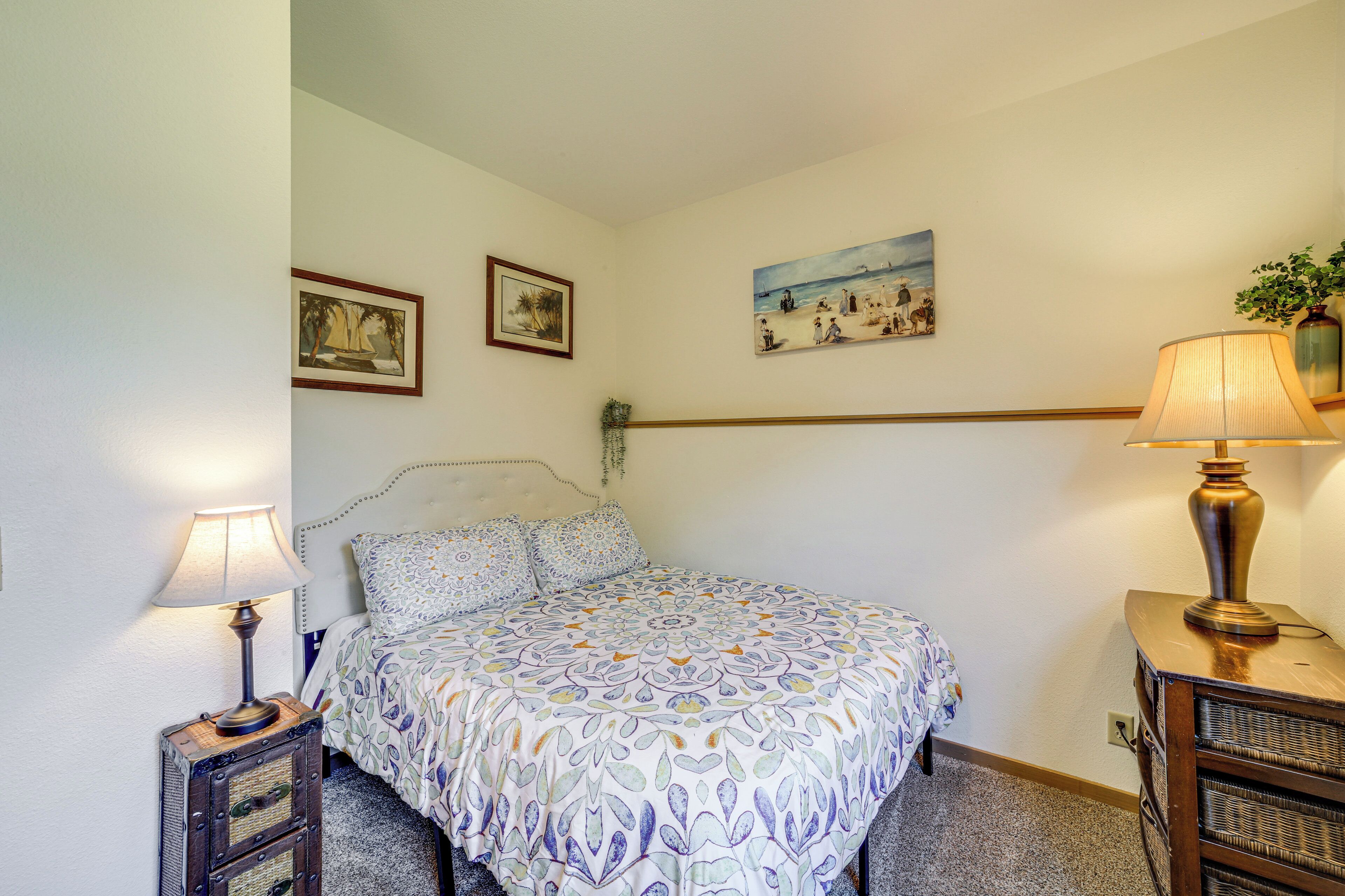 Un dormitorio con una cama, dos mesitas de noche, una lámpara y dos cuadros colgados en la pared.