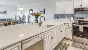 A modern kitchen with white cabinetry, a large island with a sink, and a stainless steel oven. - Oak Island Beachfront Condo w/ Community Pool (Oak Island)