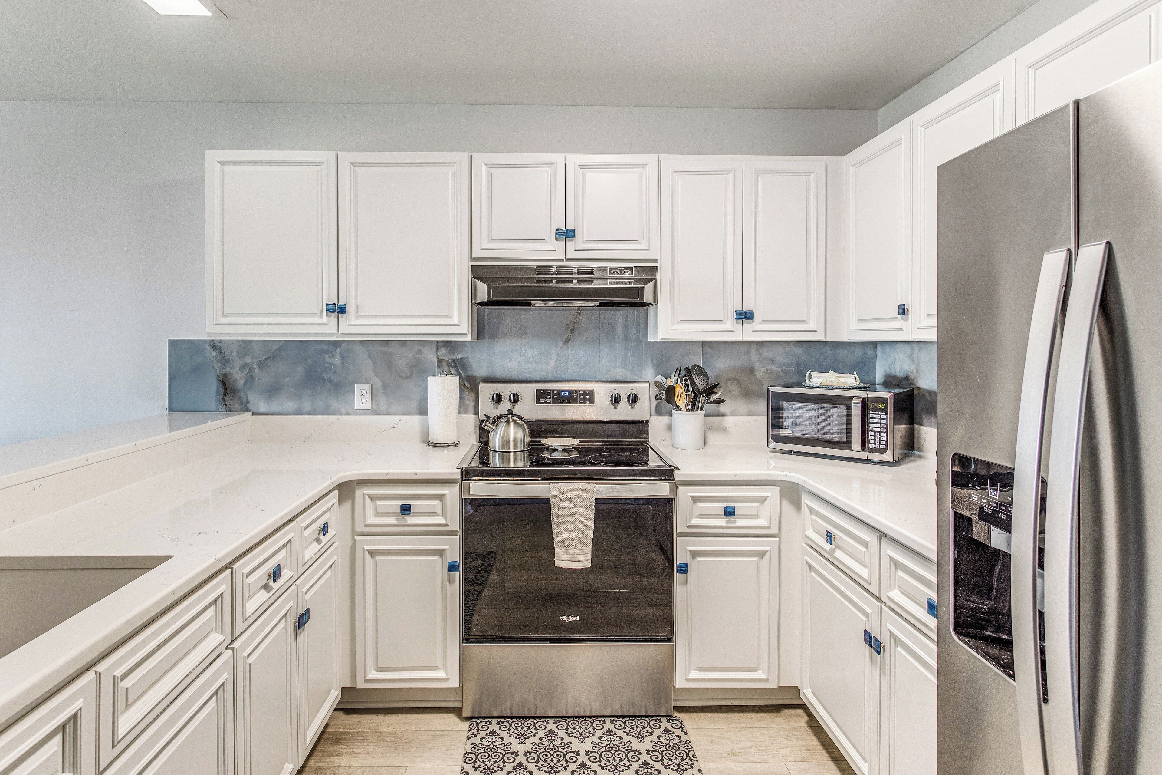 A kitchen with white cabinets, a stainless steel refrigerator, a microwave, and an oven.