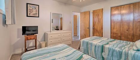 Quarto com duas camas, ventoinha no teto, televisão, cômoda e armários de madeira.