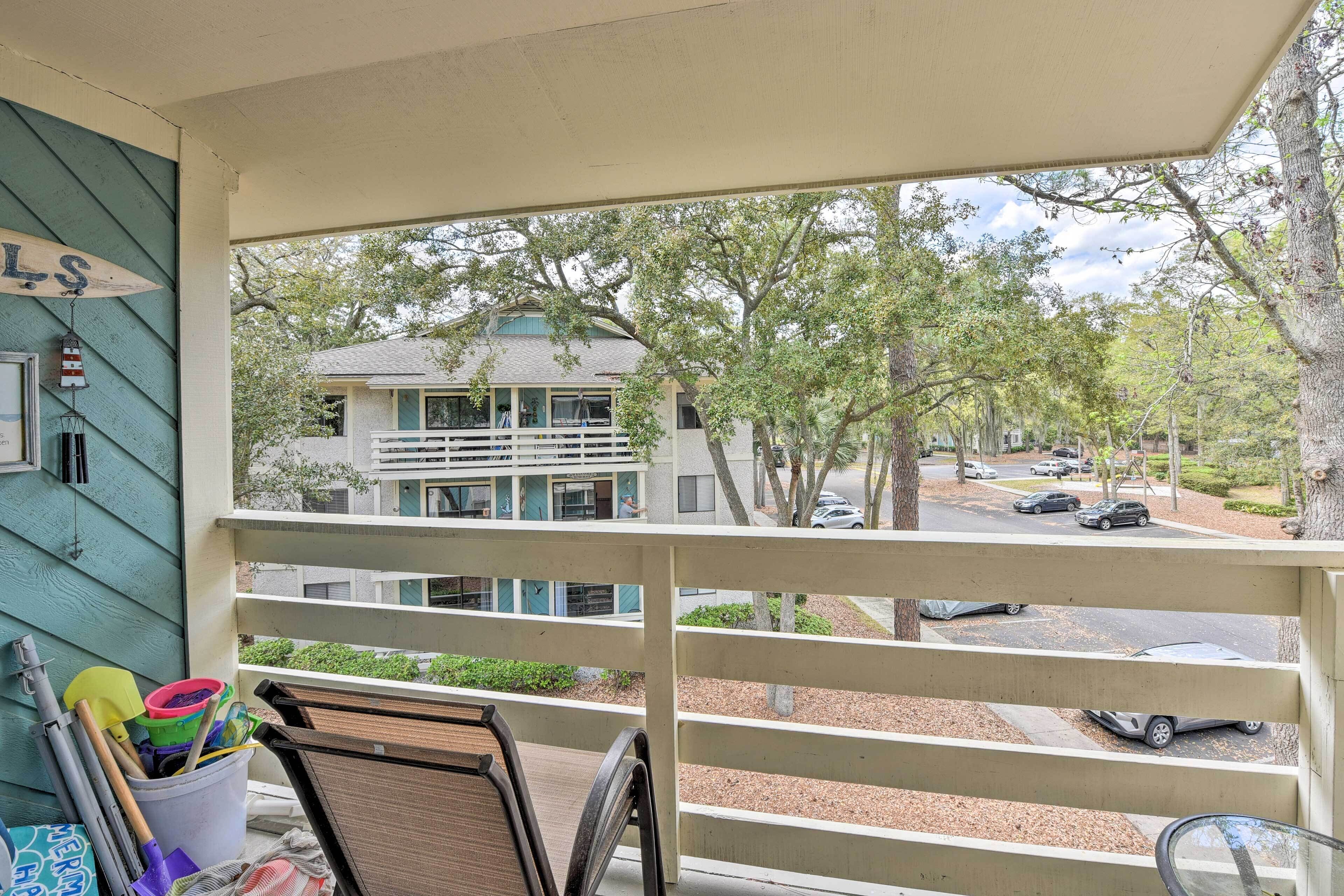 A balcony with a view of a street and buildings. There are chairs and a bucket with cleaning supplies on the balcony.