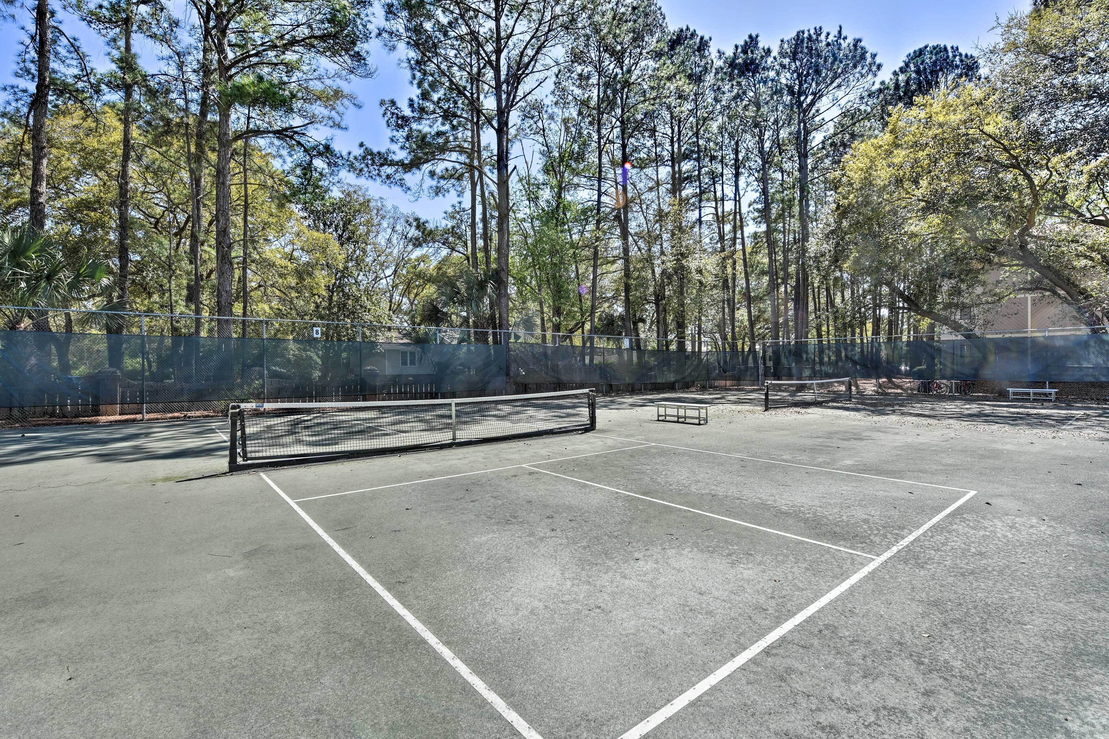 An outdoor tennis court surrounded by tall trees.