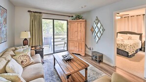 Una sala de estar acogedora con un sofá, una mesa de centro de madera y un ventanal corredero que da a un balcón.