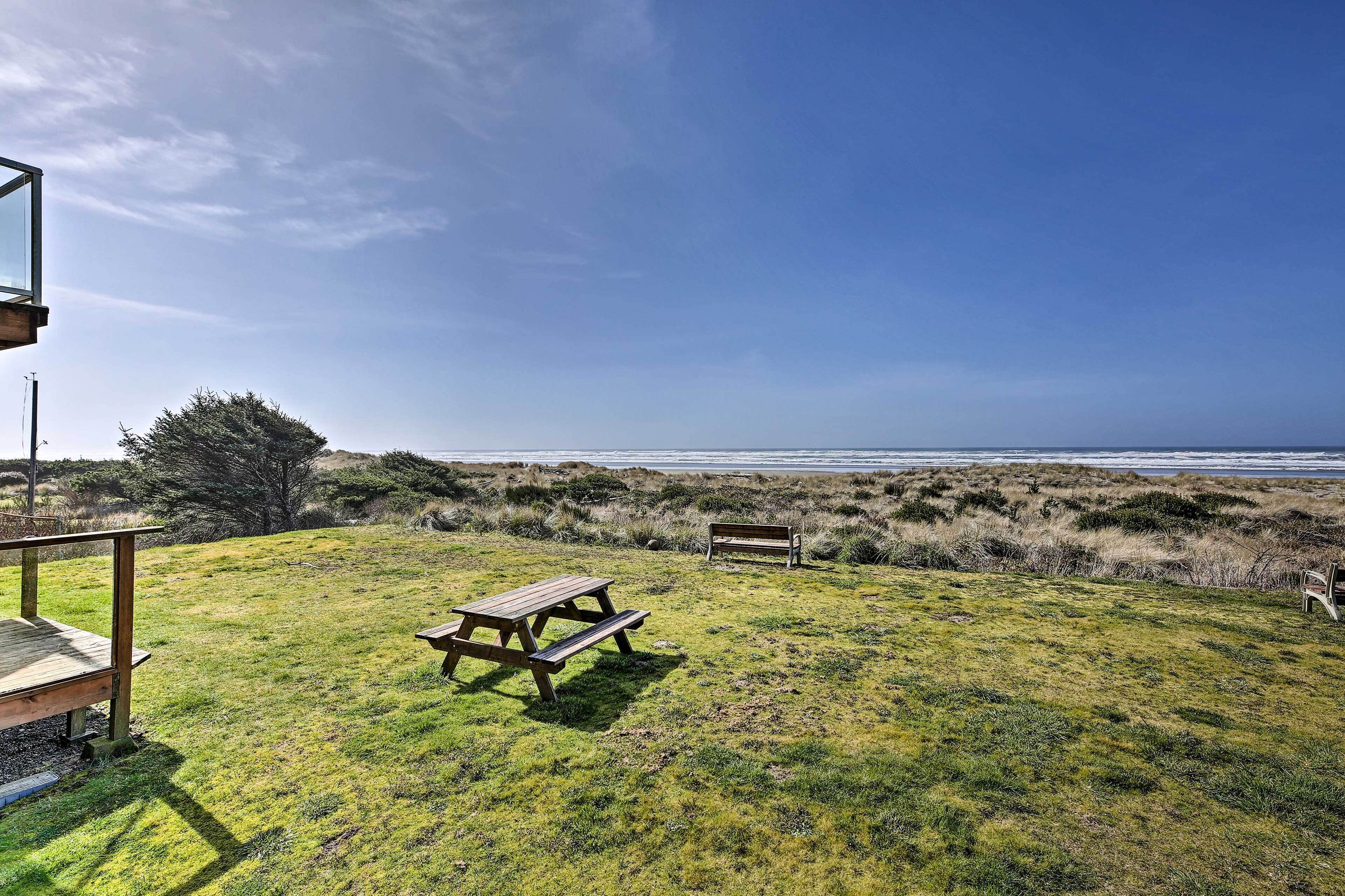 A grassy area with a wooden picnic table and bench, overlooking a beach.