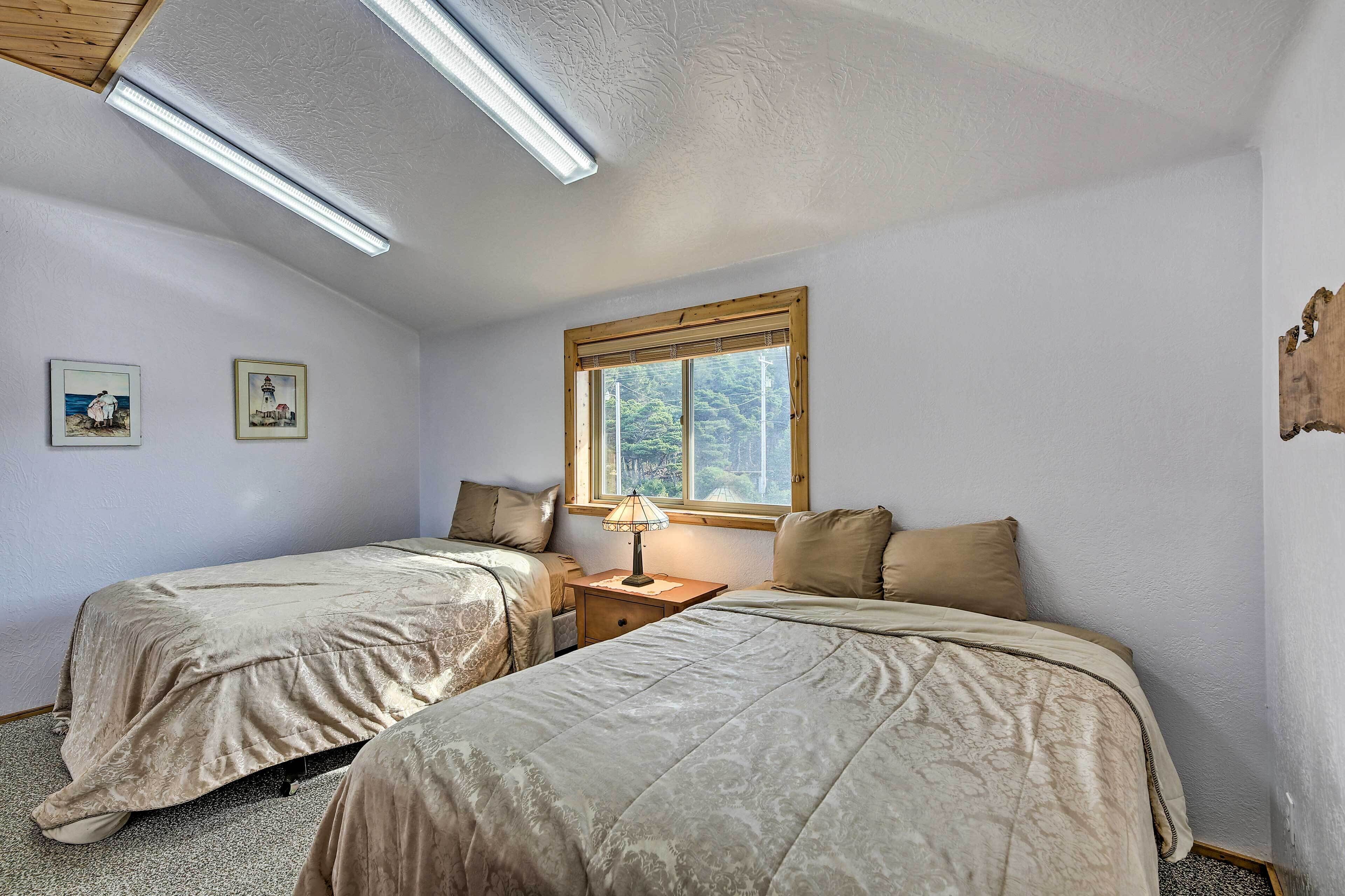 A bedroom with two beds, a window, and a nightstand with a lamp.