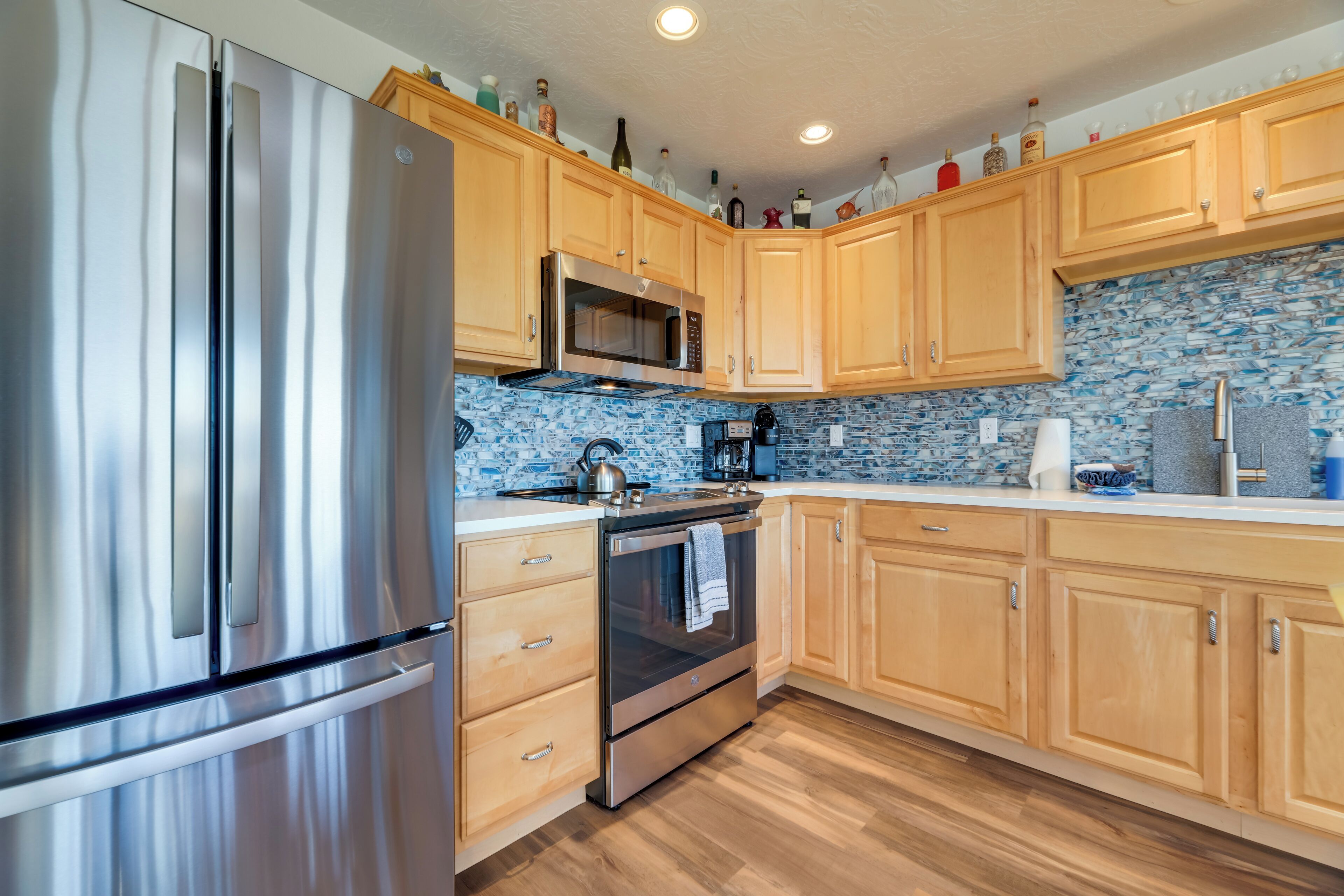 A kitchen with stainless steel appliances, wooden cabinets, and a blue mosaic backsplash.