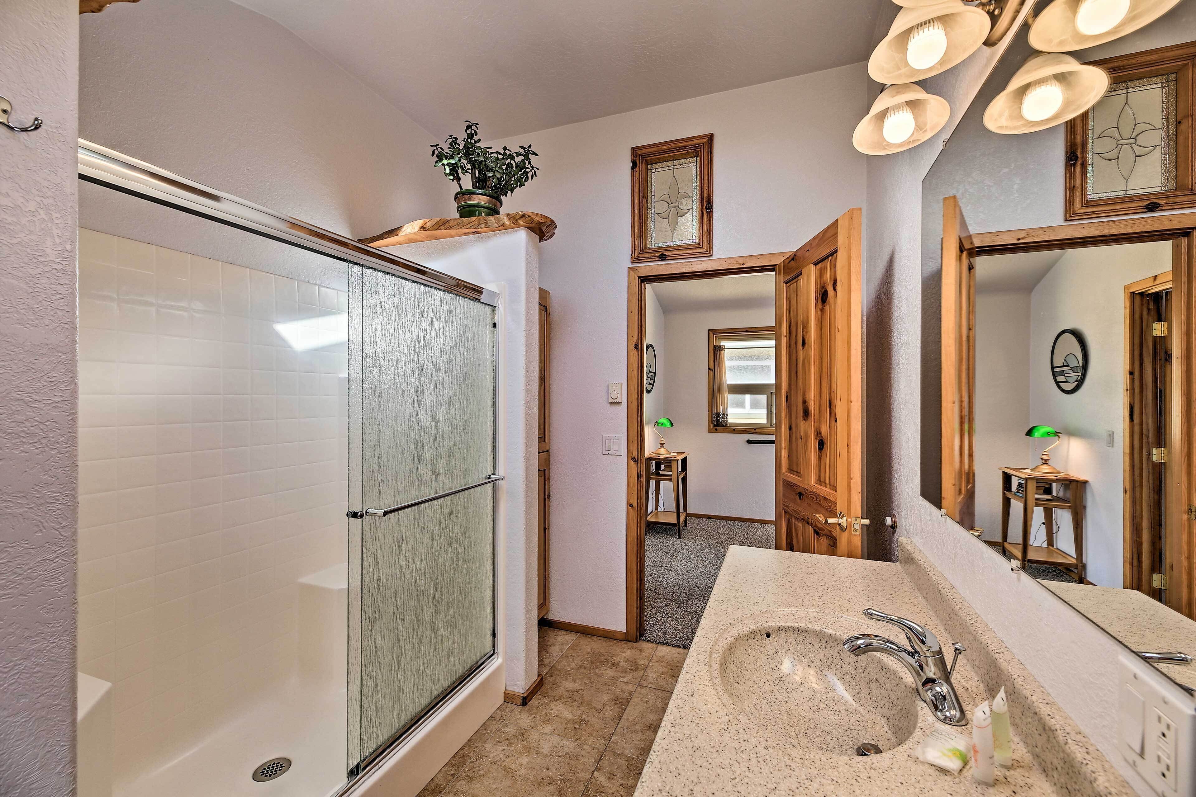 A bathroom with a glass shower enclosure, a sink with a mirror, and wooden doors.