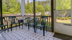A covered outdoor area with a patio, green plastic chairs, and a view of a wooded area through large windows. - Sunny Apex Vacation Rental w/ Pool Access! (Apex)