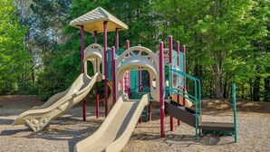 A playground with slides and climbing structures, surrounded by trees. - Sunny Apex Vacation Rental w/ Pool Access! (Apex)