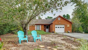 Ein Holzhaus mit Garage, zwei türkisfarbenen Adirondack-Stühlen und einem Baum im Garten.