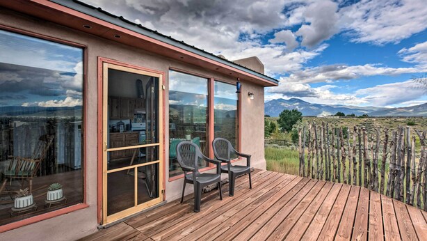 A wooden deck with two chairs, a glass door leading to a kitchen, and a view of mountains. - El Prado Duplex w/ Deck + Grill - 4 Mi to Town! (Taos)
