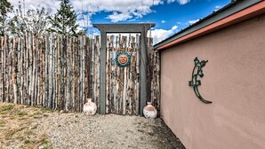 A rustic wooden gate with a decorative emblem, a wall with a crescent moon design, and a clear blue sky. - El Prado Duplex w/ Deck + Grill - 4 Mi to Town! (Taos)