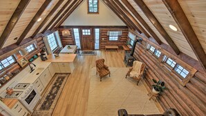 A spacious loft-style room with a high ceiling, wooden beams, a large window, a fireplace, and a cozy seating area. - Serene Kootenai Cabin - 3 Mi to Dtwn & River! (Bonners Ferry)