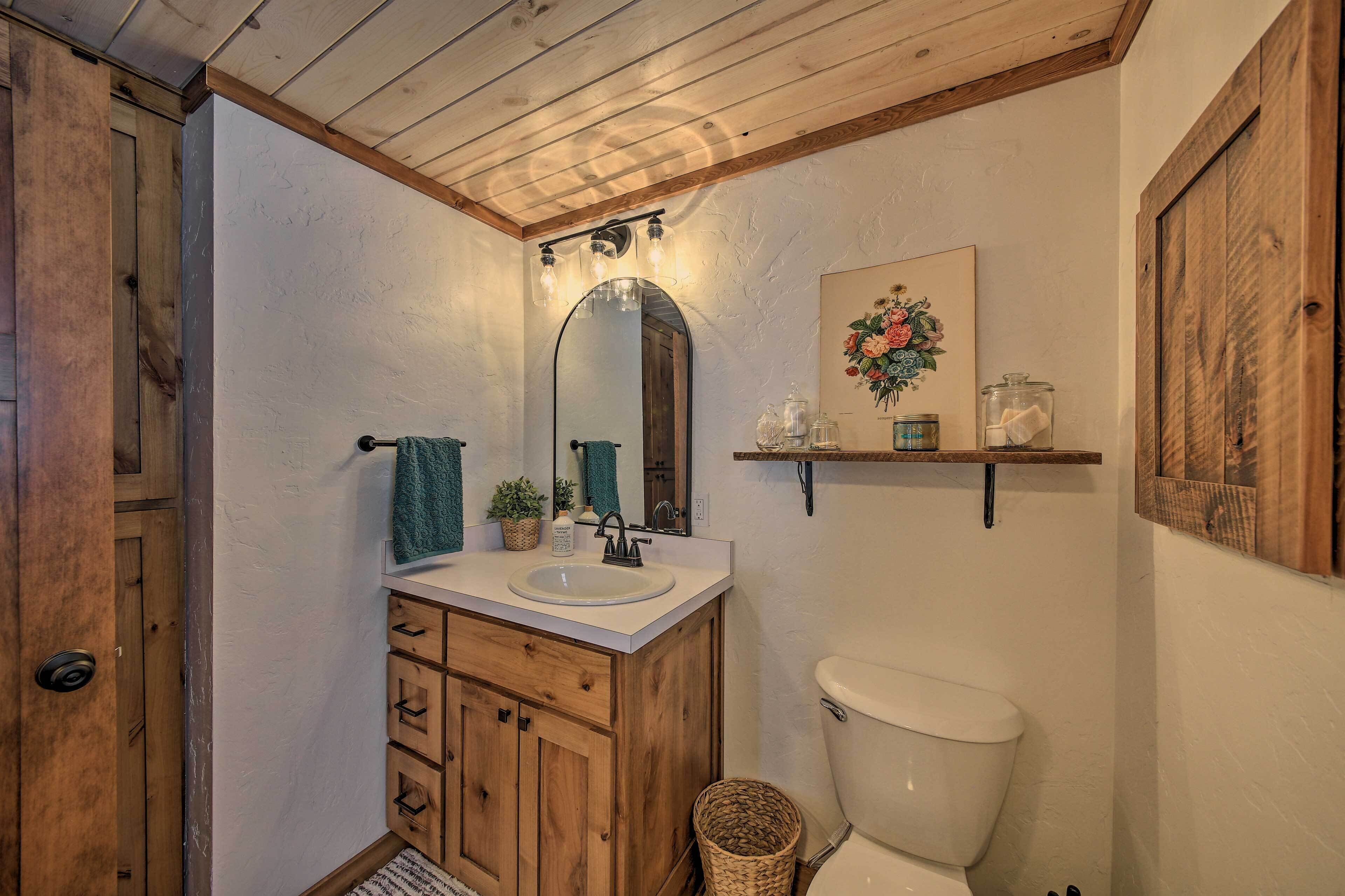 Ein Badezimmer mit Holzschränken, einem weißen Waschbecken, einem Spiegel, einer Toilette und einem Regal mit Dekoration.