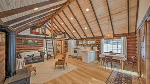 A log cabin interior with a fireplace, wooden floors, a dining area, and a kitchen. - Serene Kootenai Cabin - 3 Mi to Dtwn & River! (Bonners Ferry)