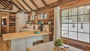 A rustic cabin kitchen with wooden beams, a wooden countertop, and a large window overlooking a snowy landscape. - Serene Kootenai Cabin - 3 Mi to Dtwn & River! (Bonners Ferry)