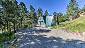 A building with a sloped roof and a metal facade, surrounded by a gravel driveway and a wooden fence. - Cloudcroft Cabin w/ National Forest Views! (Cloudcroft)