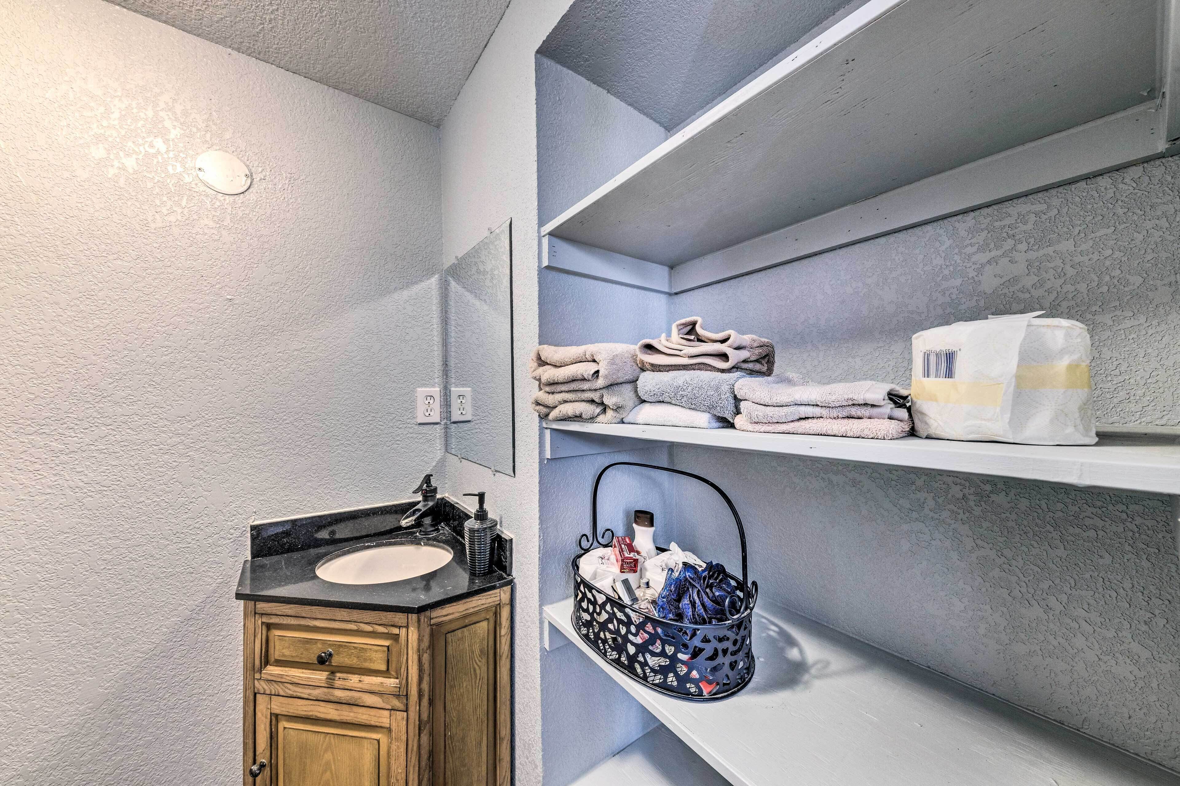 A bathroom with a wooden vanity, a sink, a mirror, and shelves with towels and a basket.