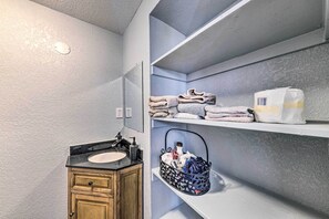 Une salle de bain avec un meuble-lavabo en bois, un évier, un miroir et des étagères où sont rangées des serviettes et un panier.