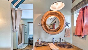 Un baño con tocador de madera, espejo redondo, lavabo y un perchero con forma de estrella.