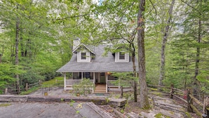 A two-story house with a porch, surrounded by a forest.