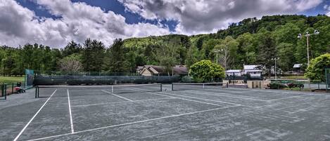 A tennis court with a net, surrounded by trees and a hill in the background.