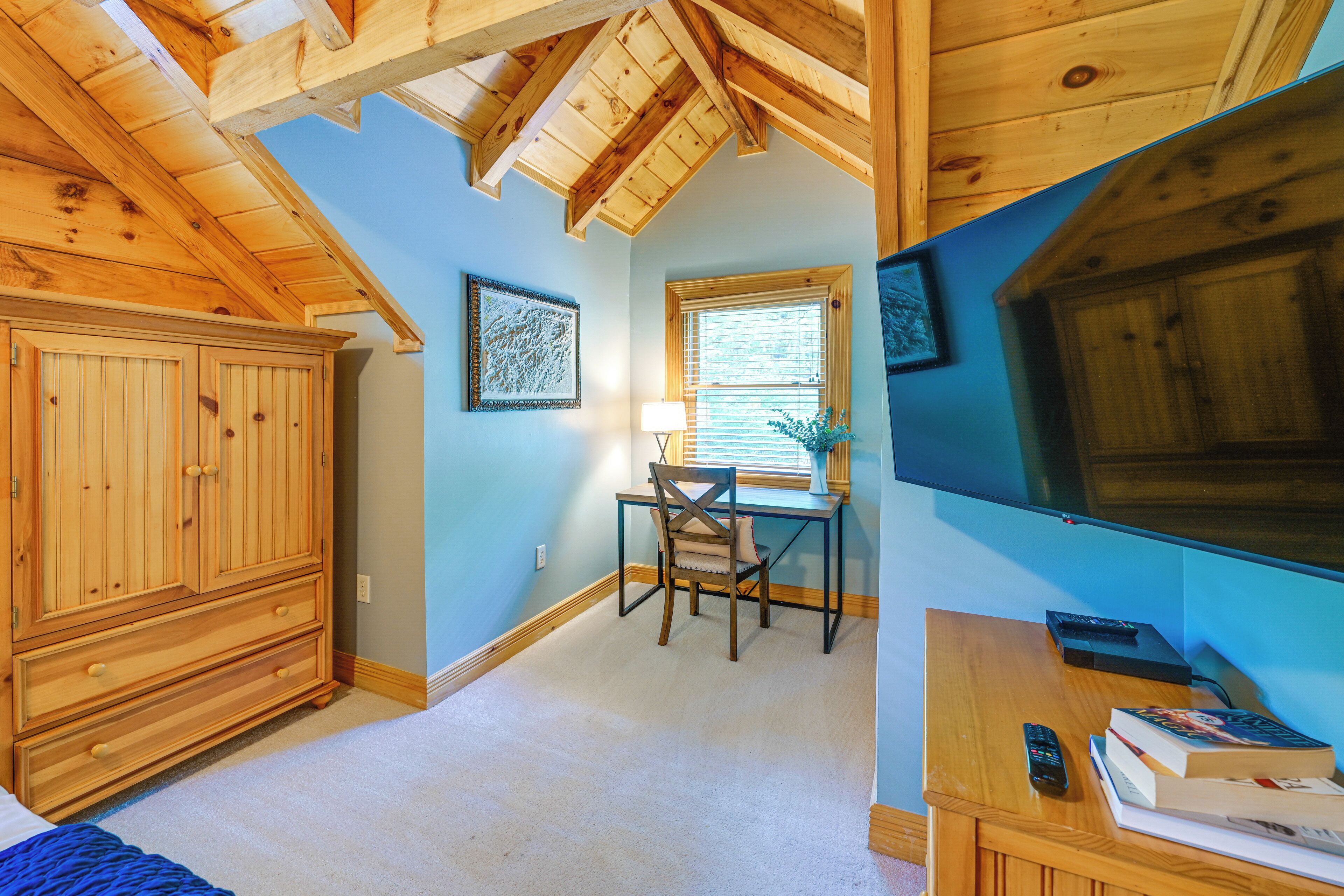 A bedroom with a wooden ceiling, a desk with a chair, a TV, and a wardrobe.
