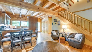 A spacious living area with a wooden ceiling, a dining table with chairs, a leather armchair, and a staircase.