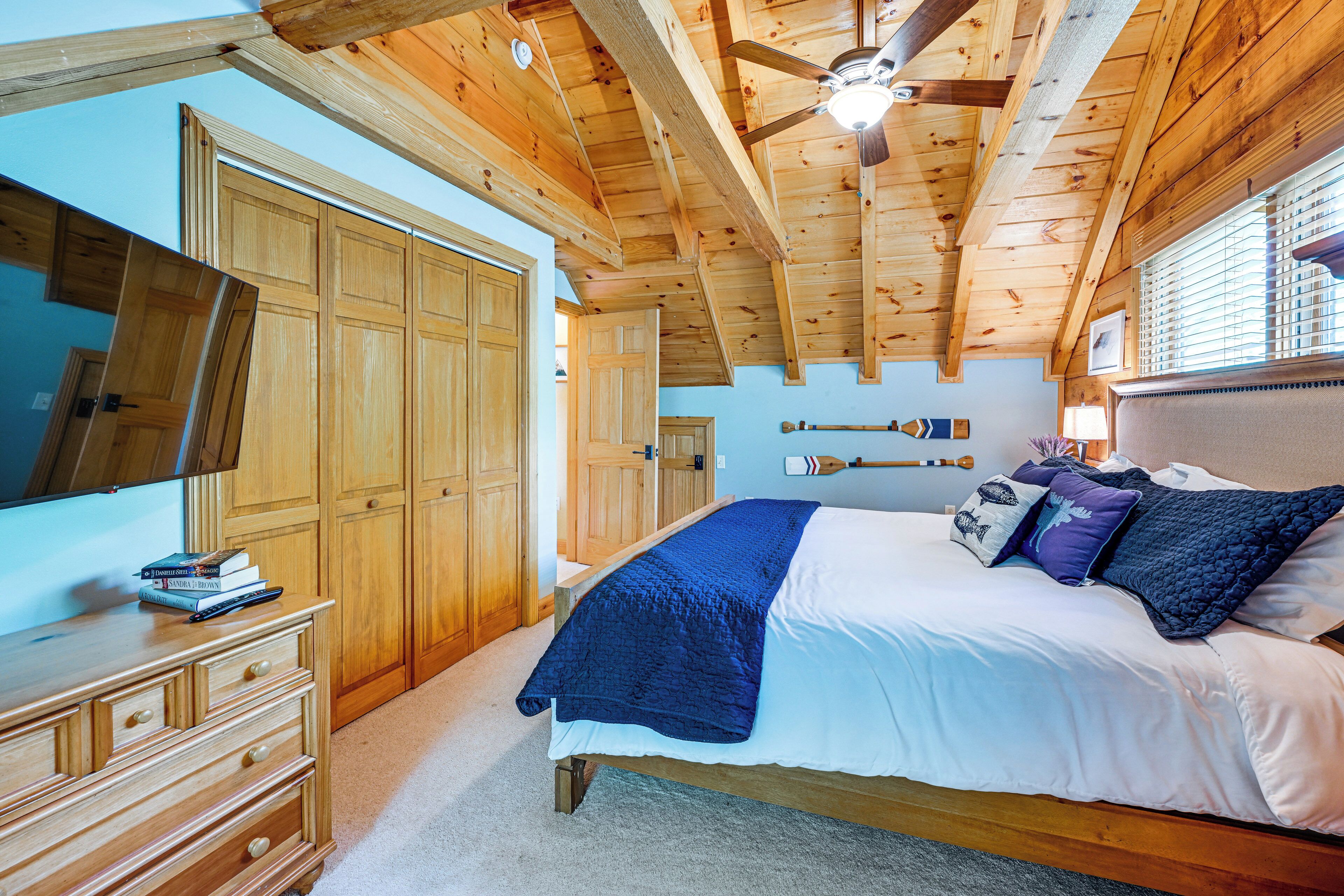 Een slaapkamer met een houten plafond, een bed met wit en blauw beddengoed, een houten dressoir en een grote spiegel.