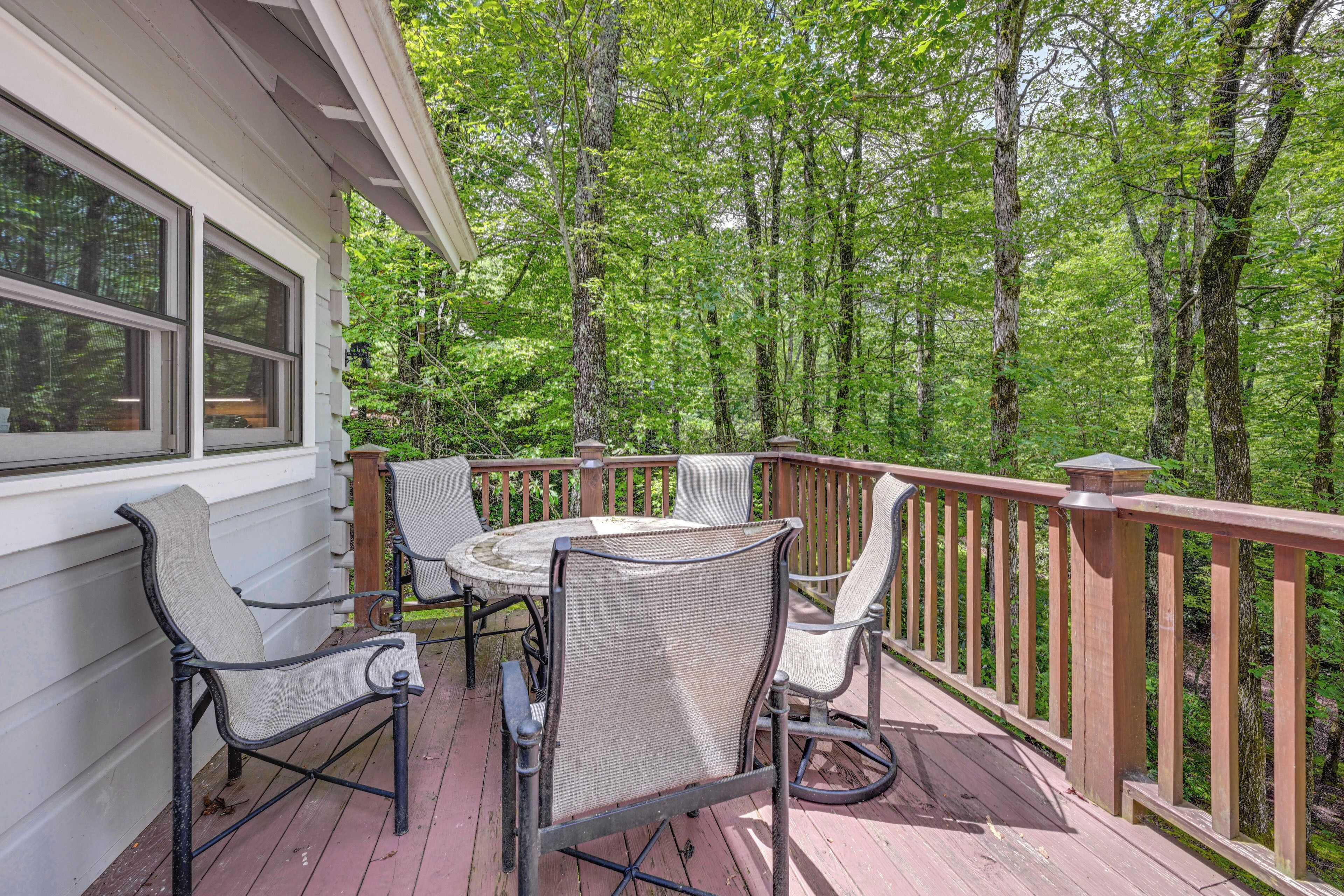 A wooden deck with outdoor furniture, surrounded by a wooden railing and dense trees.