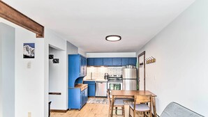 Cocina compacta con armarios azules, una mesa de comedor de madera y un sofá gris.