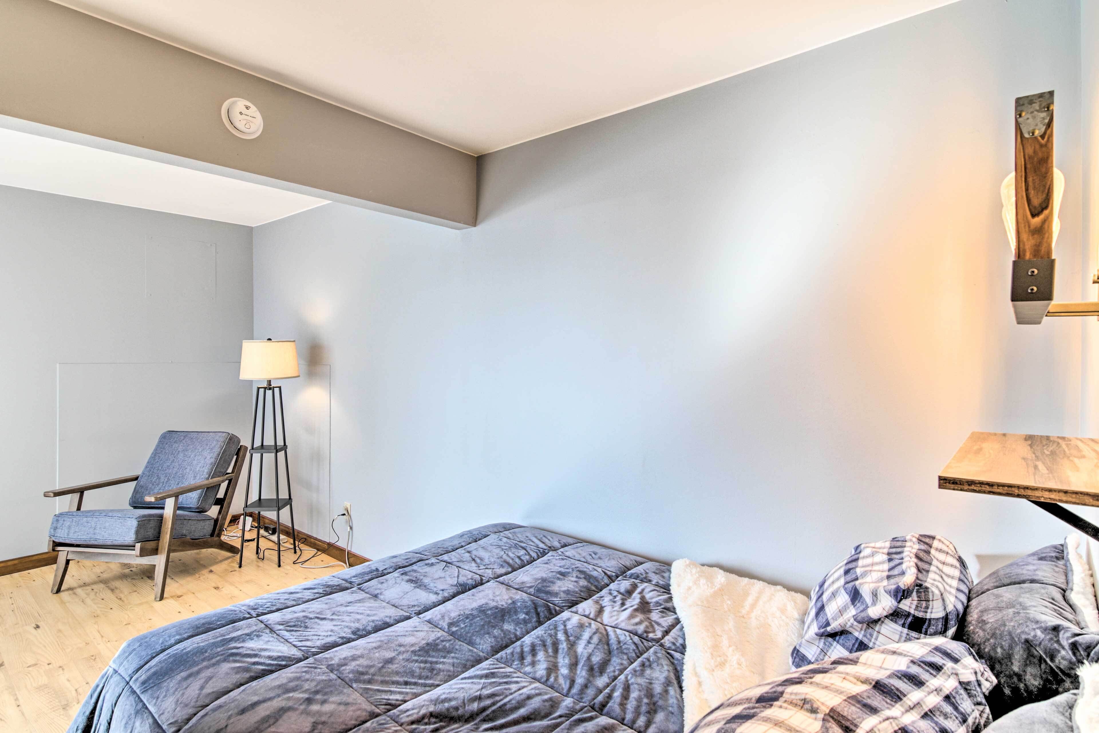 Une chambre à coucher comprenant un lit, une chaise, une lampe sur pied et un luminaire fixé au mur.