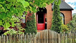 A brick house with a red door, surrounded by a wooden fence and greenery. - Ski, Shop & Explore: Walkable Midtown Reno Oasis! (Reno)