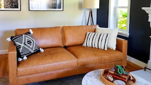 A brown leather sofa with patterned pillows, a side table with a woven tray, and framed artwork on the wall. - Ski, Shop & Explore: Walkable Midtown Reno Oasis! (Reno)