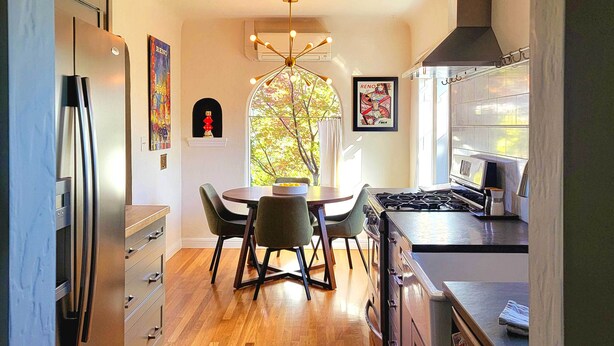 A modern kitchen with a stainless steel refrigerator, a dining table with chairs, a gas stove, and a window with a view of trees. - Ski, Shop & Explore: Walkable Midtown Reno Oasis! (Reno)