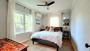 A bedroom with a bed, a ceiling fan, a nightstand, a lamp, and a window with curtains. - Ski, Shop & Explore: Walkable Midtown Reno Oasis! (Reno)