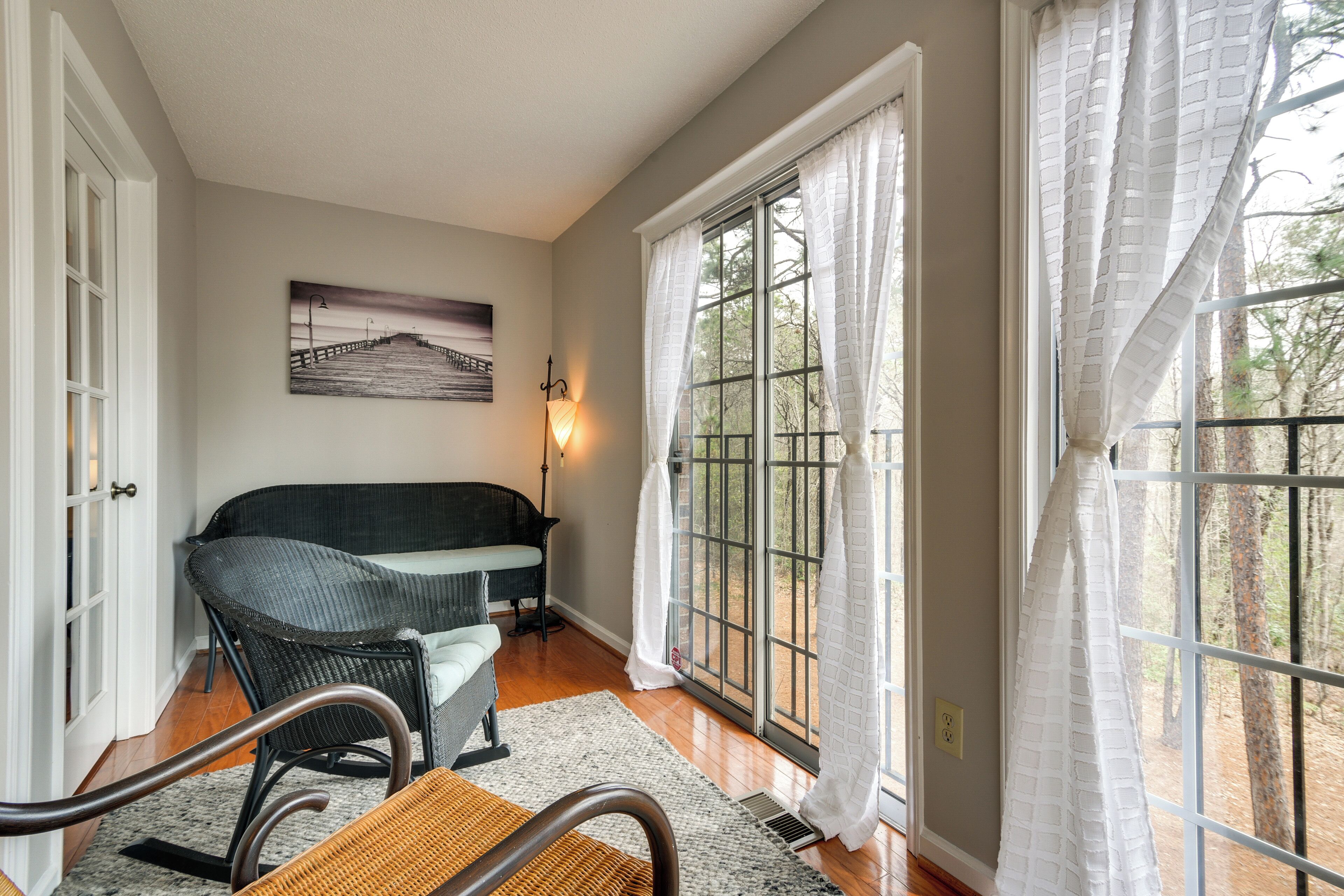 A room with a sofa, a chair, a rug, a painting, and a window with curtains.
