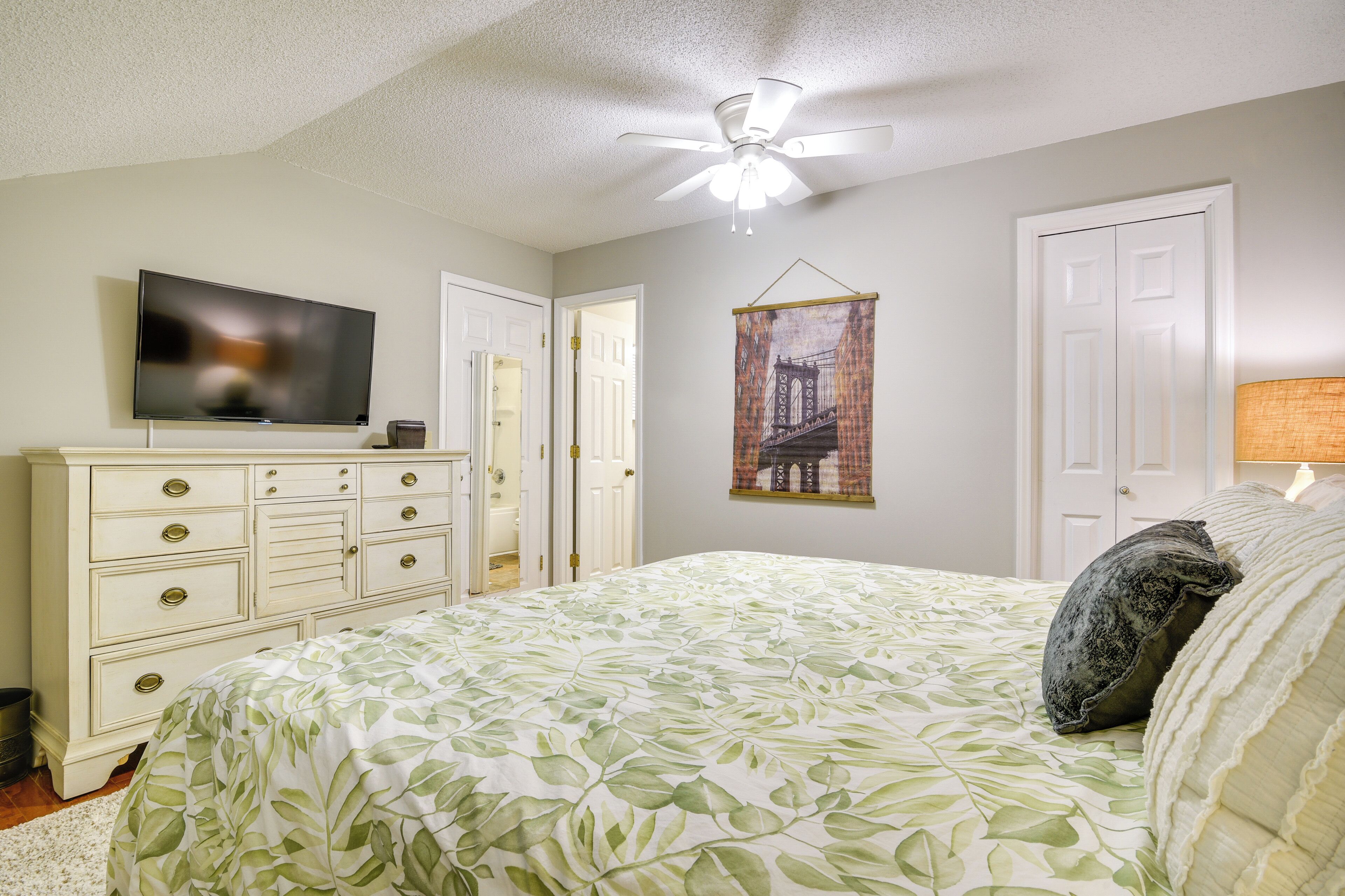 A bedroom with a bed, dresser, television, and a door leading to another room.