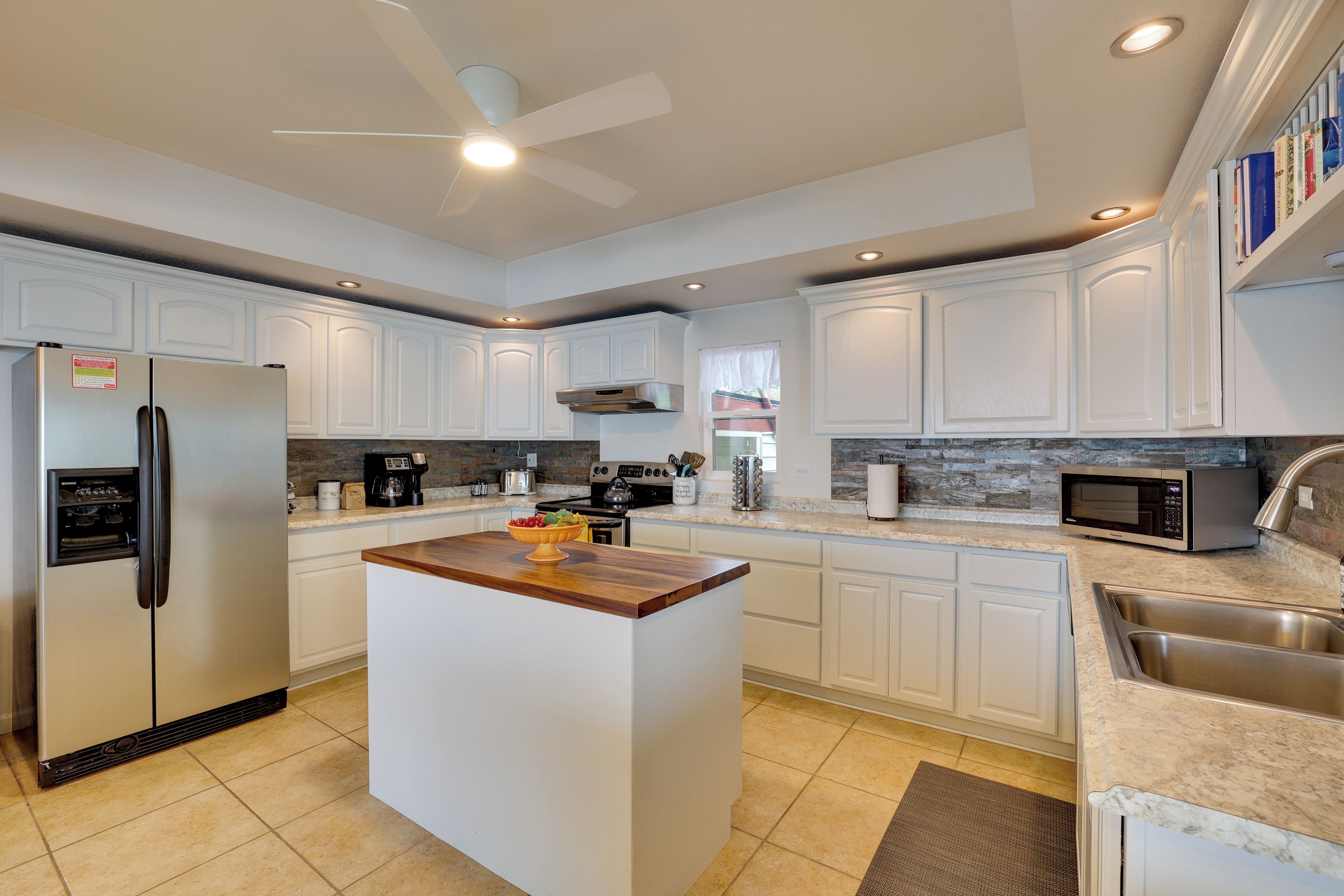 A modern kitchen with white cabinetry, a central island, stainless steel appliances, and a built-in microwave.