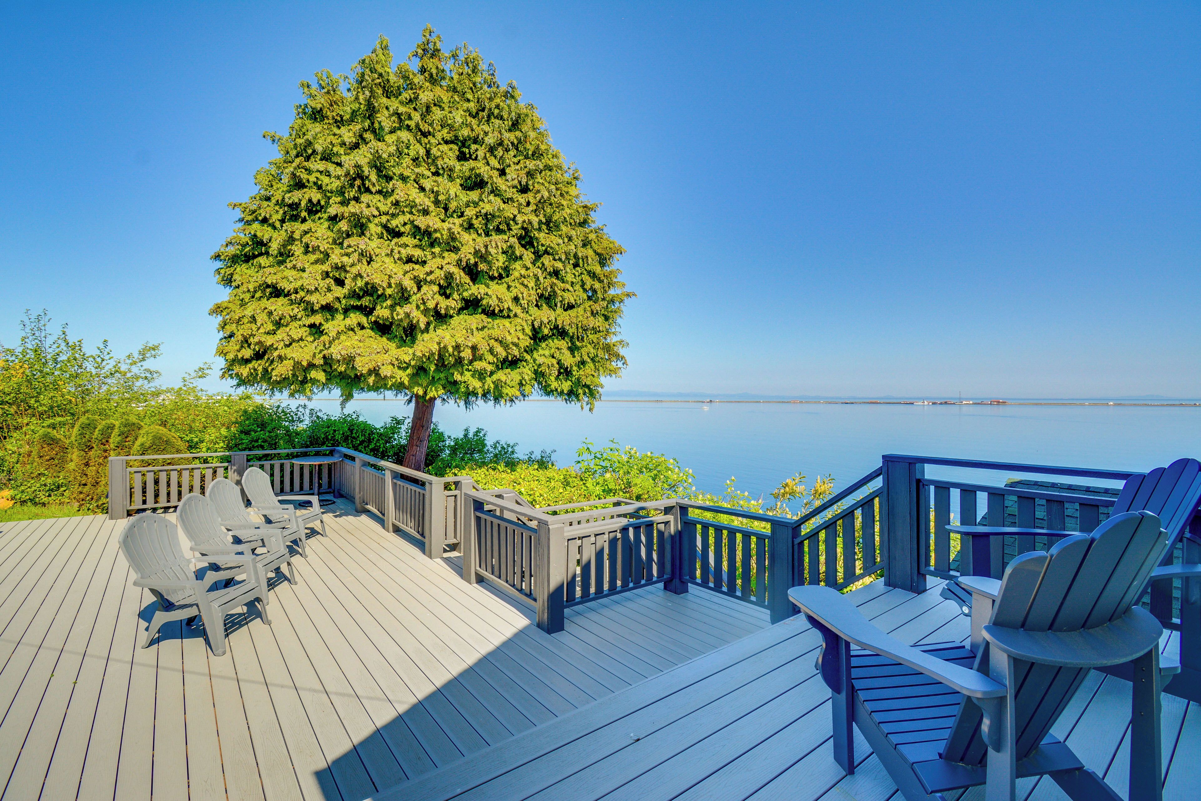A wooden deck with Adirondack chairs and a view of the water.