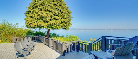 A wooden deck with Adirondack chairs and a view of the water.